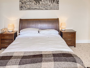 Quarto de hotel com uma cama grande, duas mesas de cabeceira com abajures, uma cabeceira e uma obra de arte pendurada na parede.