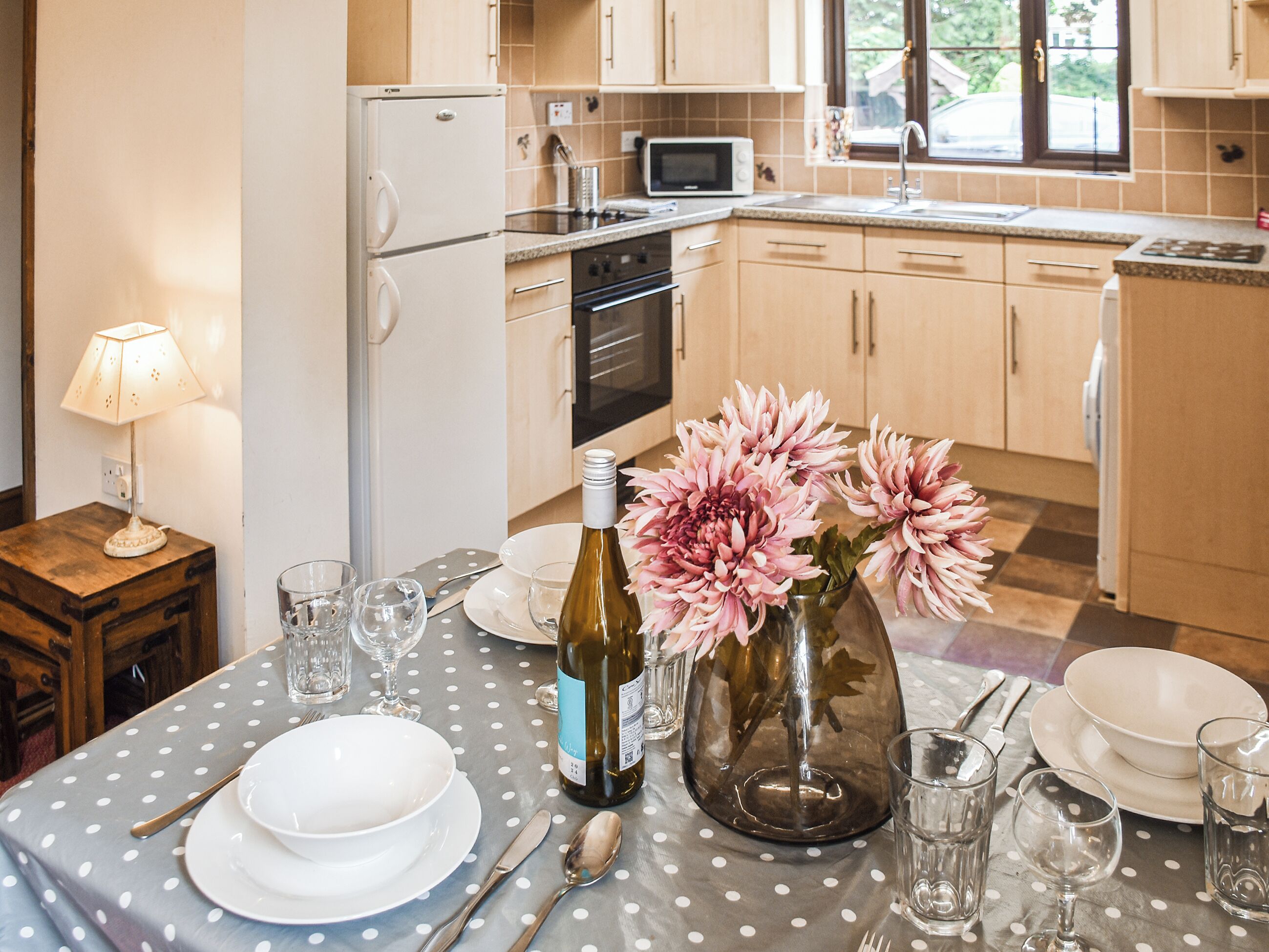 A kitchen with wooden cabinets, a microwave, and a dining table set with plates, glasses, and cutlery.