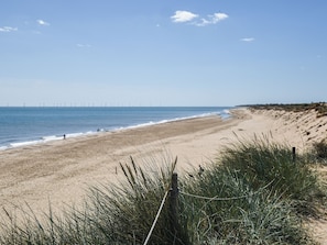A beach with a clear sky, a sandy shore, and a distant view of wind turbines. - Cherry Tree Cottage - UK52225 (Horning)