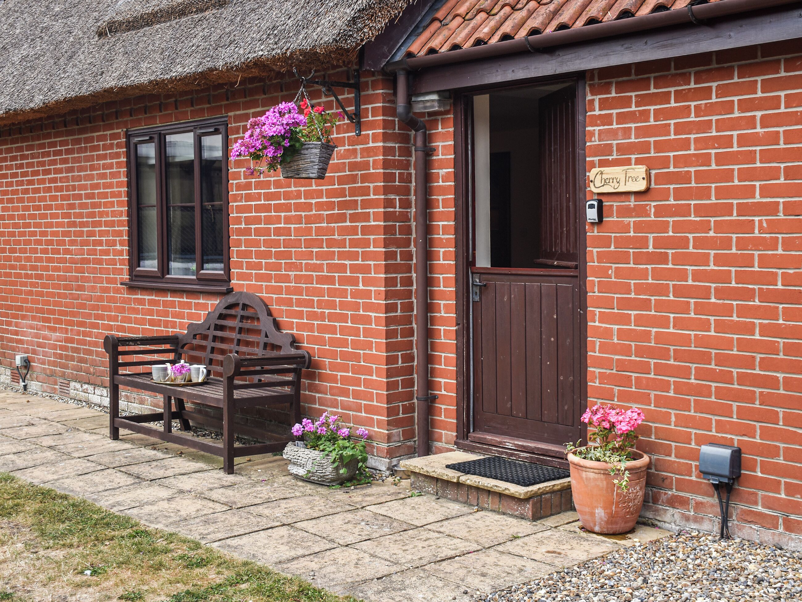 A brick house with a wooden bench, a door, and hanging flower baskets.