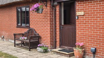 A brick house with a wooden bench, a door, and hanging flower baskets.