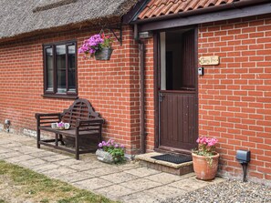 A brick house with a wooden bench, a door, and hanging flower baskets. - Cherry Tree Cottage - UK52225 (Horning)