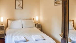 Ein ordentlich bezogenes Bett mit weißen Leinentüchern, zwei Nachttischlampen, einem Holz-Kopfteil und einem gerahmten Bild an der Wand.