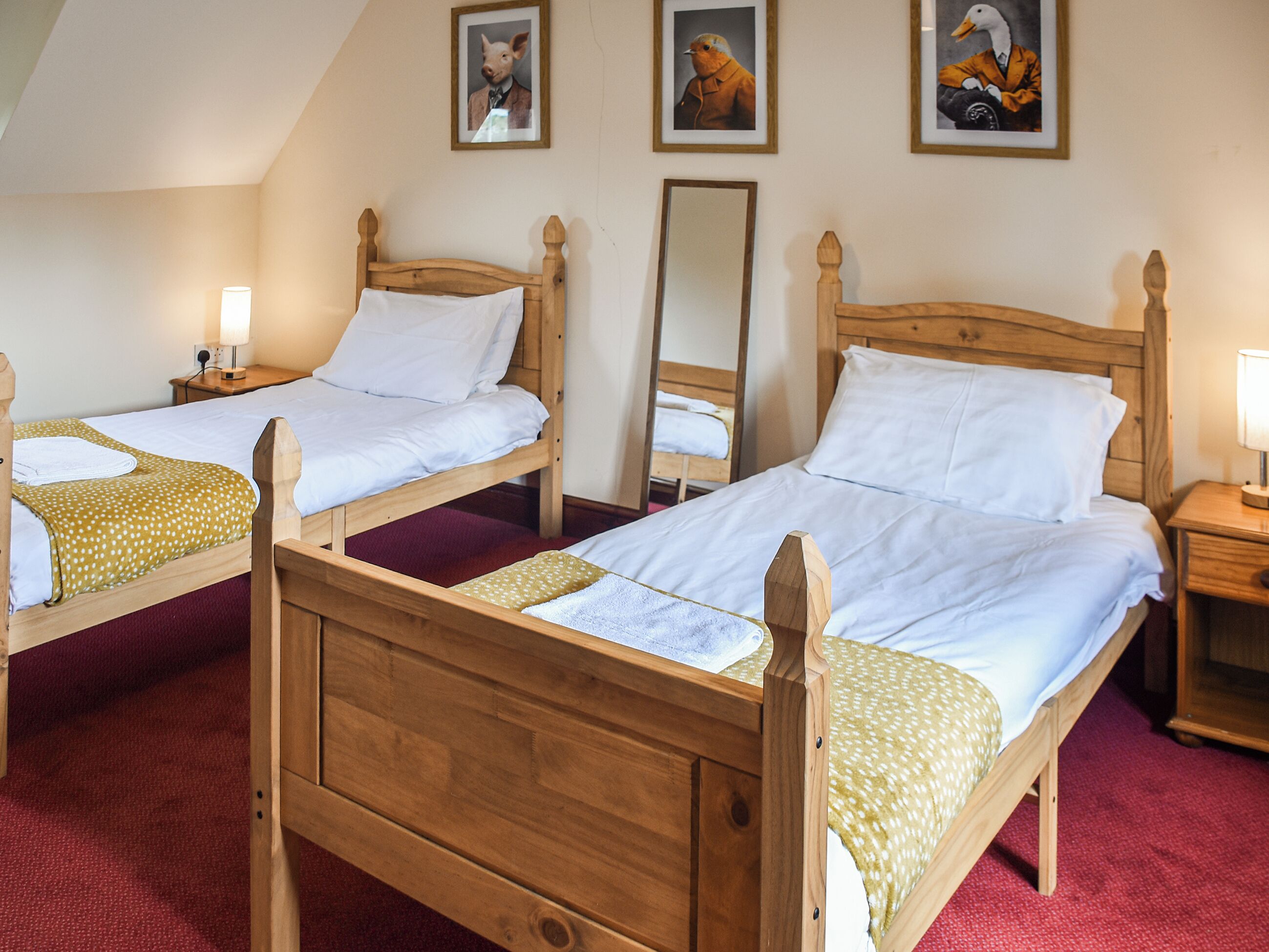 Ein Zimmer mit zwei hölzernen Betten, jeweils mit einem Nachttisch und einer Lampe. An der Wand befinden sich gerahmte Bilder.