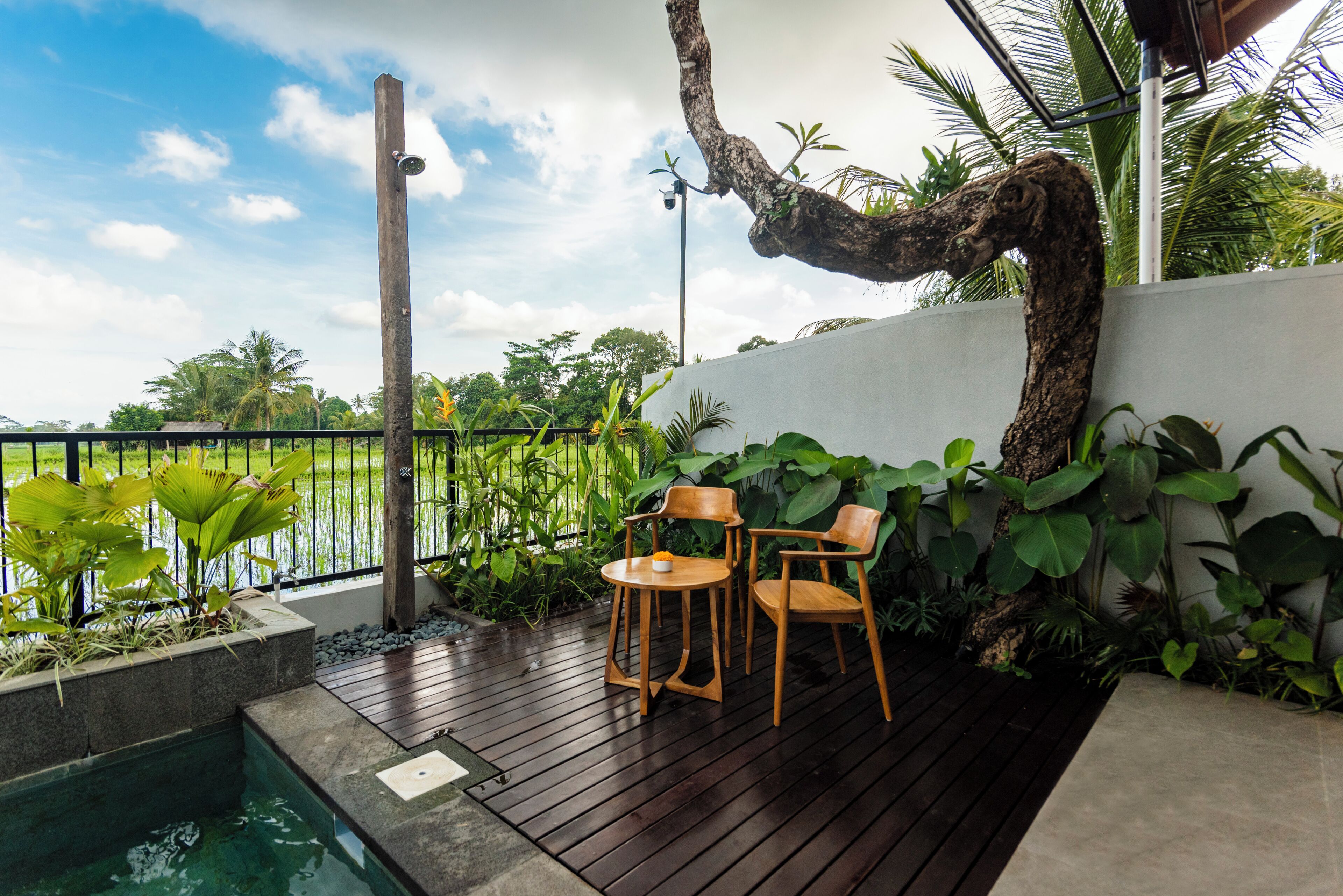 Terraza de madera con dos sillas y una mesa pequeña, con vista a una masa de agua y abundante vegetación.