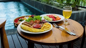 Een eettafel met borden eten en een glas drinken, met uitzicht op een zwembad.