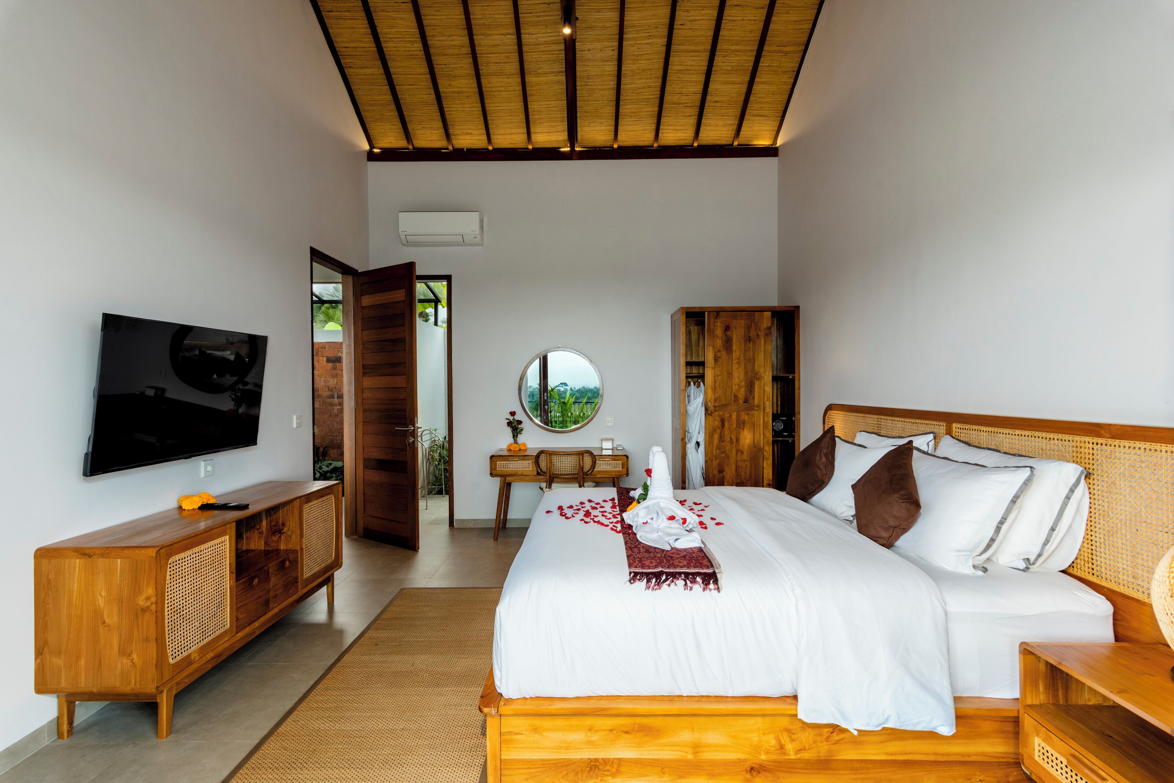 Un dormitorio moderno con una cama, un televisor, un armario de madera y vistas a través de una puerta abierta.