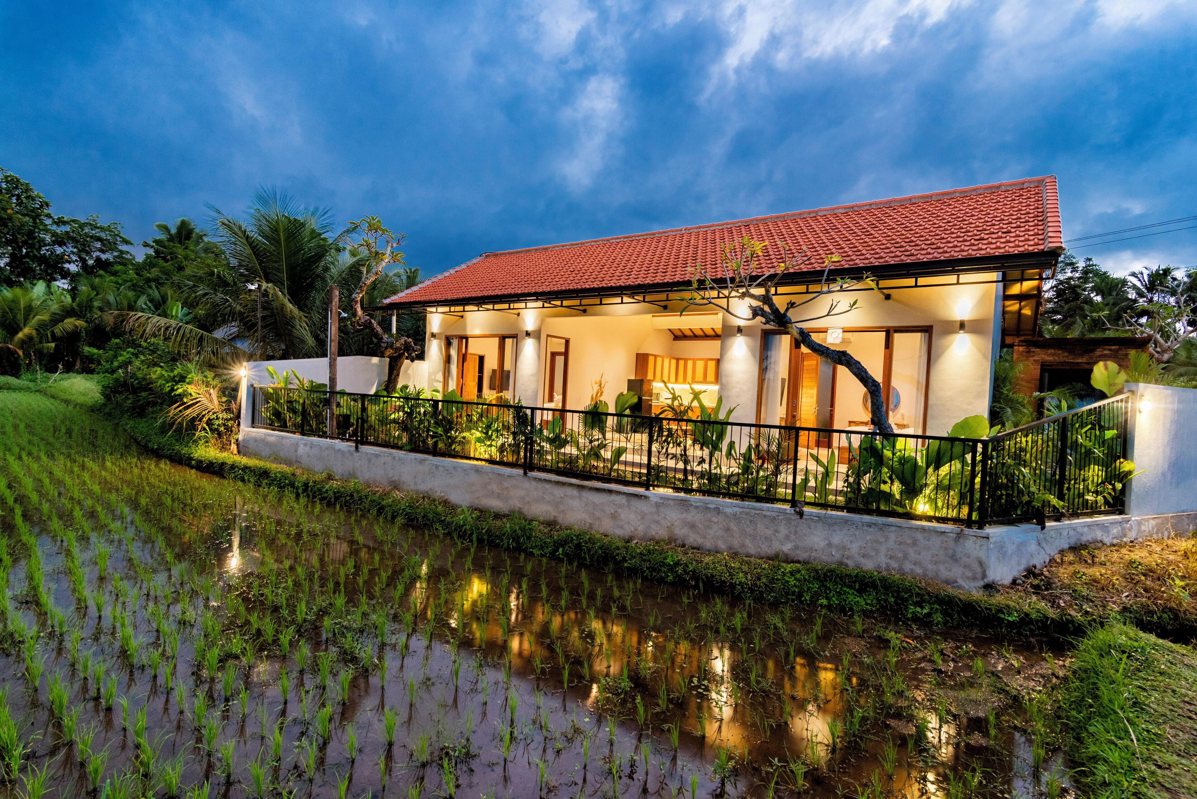 A house with a red-tiled roof, surrounded by a water body and greenery.