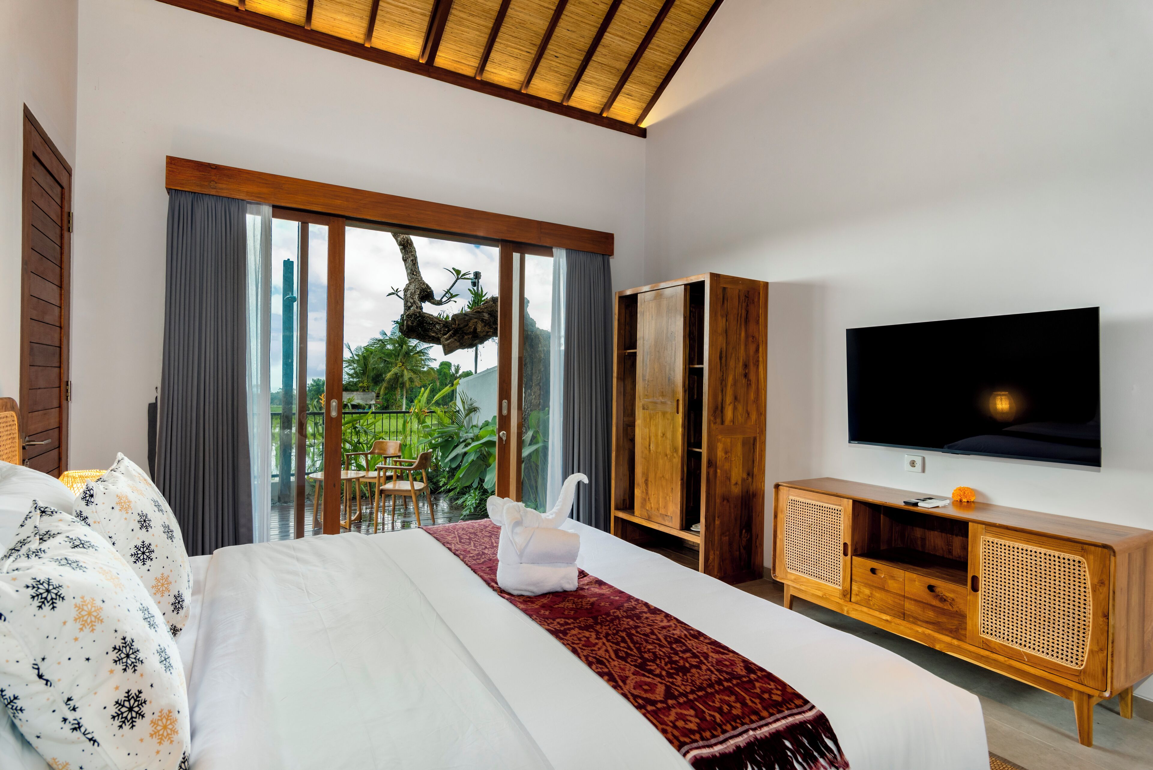 Quarto de hotel moderno com uma cama grande, televisão, armário de madeira e vista para o verde pela janela.