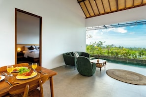 Una habitación con una mesa de comedor lista para una comida, un sofá y vistas a una piscina y follaje.