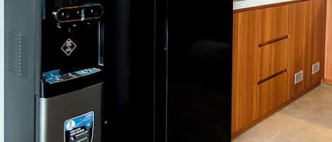 Una cocina con refrigerador negro, dispensador de agua, armarios de madera y un microondas.