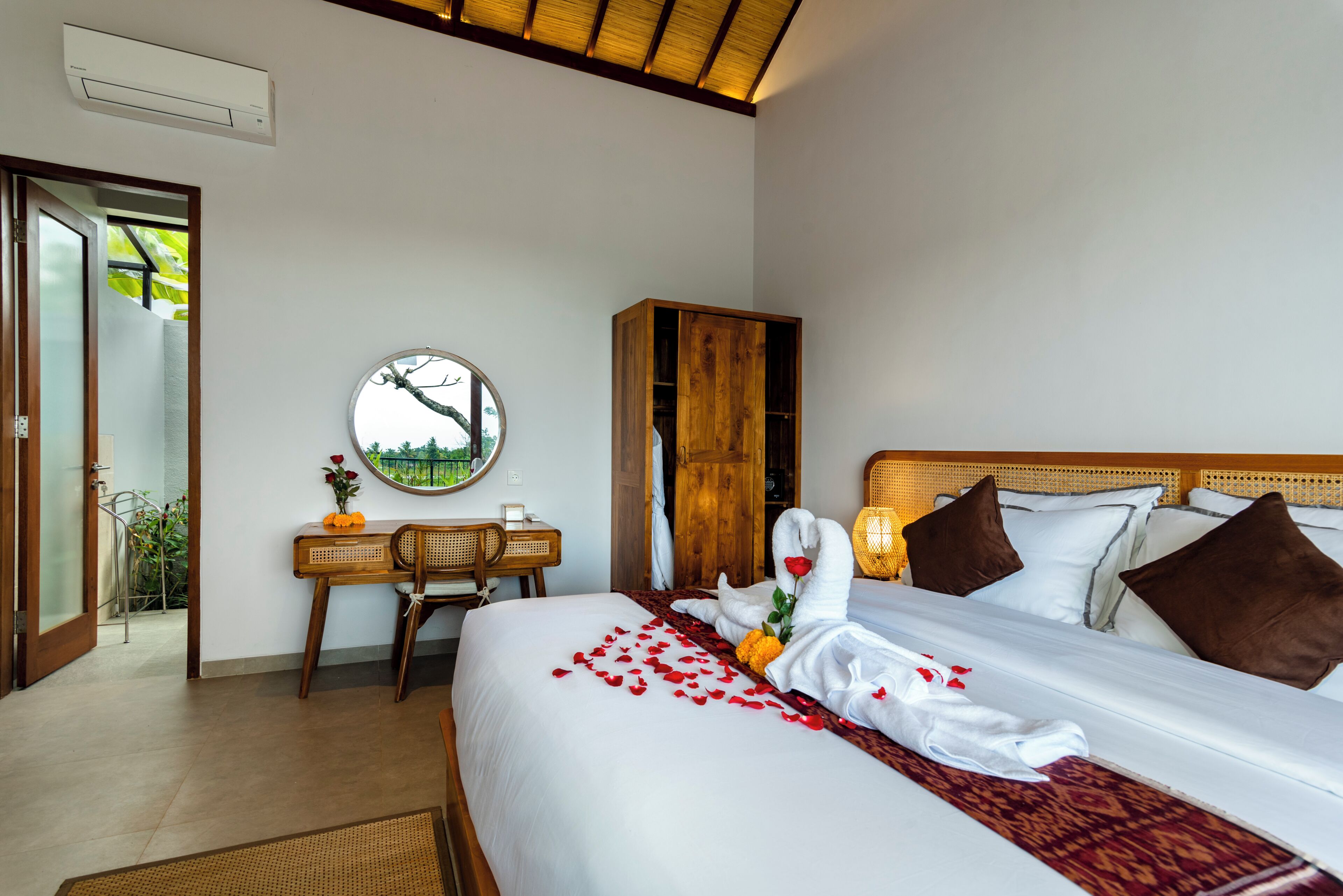 A hotel room with a bed, a desk, a chair, a wardrobe, and a round mirror on the wall.