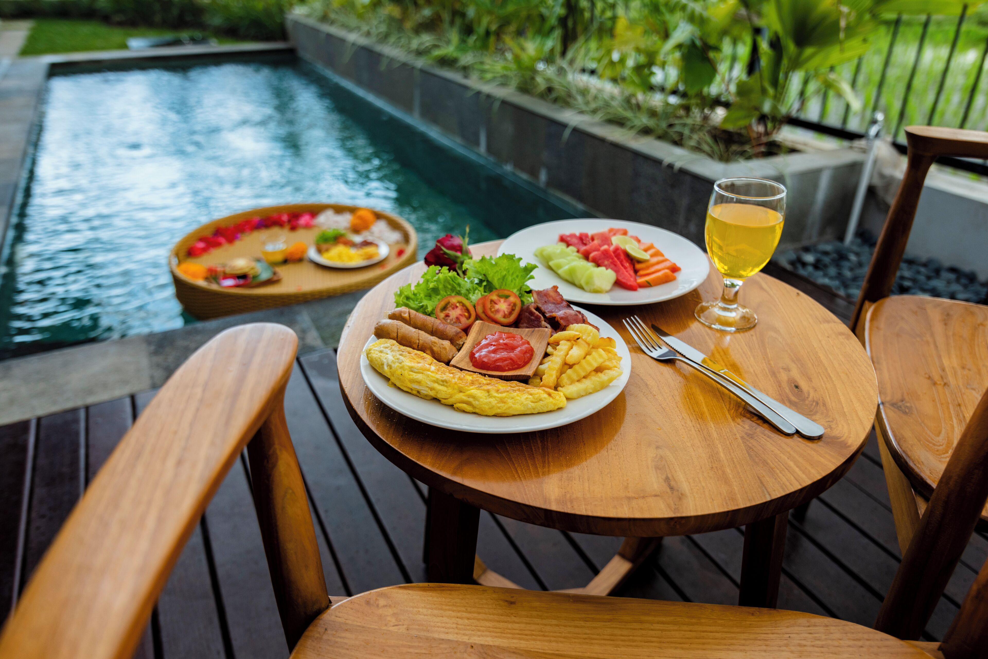 A dining table with plates of food, a glass of drink, and a pool in the background.