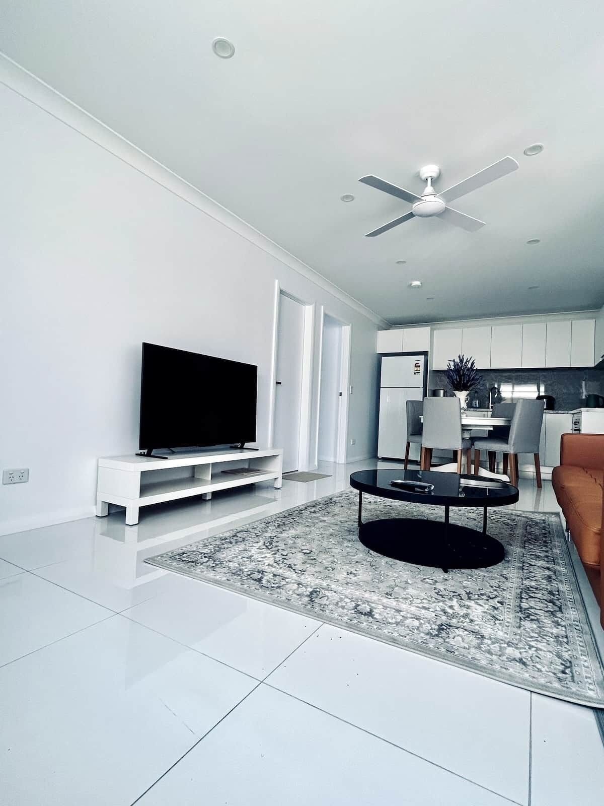 A modern living room with a flat-screen TV, a coffee table, and a ceiling fan.