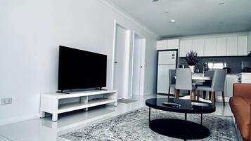 A modern living room with a flat-screen TV, a coffee table, and a ceiling fan.