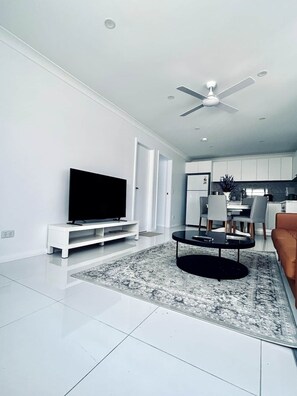 A modern living room with a flat-screen TV, a coffee table, and a ceiling fan.