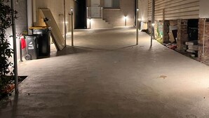 Un espacio al aire libre techado, con piso de concreto y una escalera que conduce a un edificio.