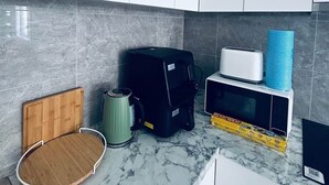 Una cocina con armarios blancos, una tabla de cortar de madera, una cafetera, un electrodoméstico negro, un tostador y un microondas sobre una encimera de mármol.