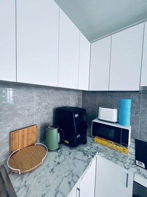 A kitchen with white cabinets, a wooden cutting board, a coffee maker, a black appliance, a toaster, and a microwave on a marble countertop. - New 2BR1B Flat+2 Free parking|Lake nearby&Hospital (North Parramatta)