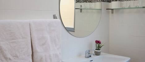 Une salle de bain avec un lavabo blanc, un miroir rond et deux serviettes accrochées au mur.