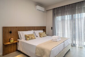 Habitación de hotel moderna con una cama grande, una mesita de noche con lámpara y una ventana con cortinas.
