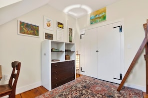 Una habitación con un armario blanco, una silla de madera, un tapete estampado y obras de arte en las paredes.