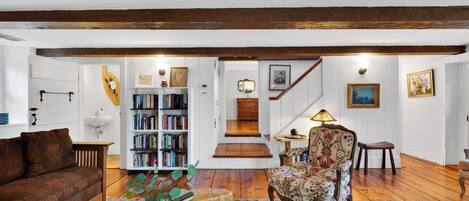 Una sala de estar acogedora con piso de madera, una estantería, un sillón estampado y una escalera que sube a otro nivel.