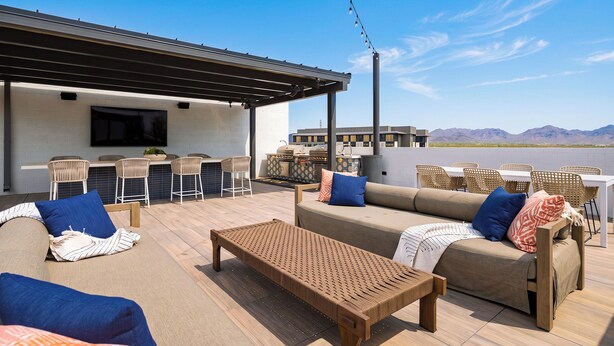 An outdoor patio with a sofa, chairs, a table, and a grill area. - Desert Ridge Condo • Shared Rooftop Pool + Sauna + Mountain Views | Azur #245 (Phoenix)