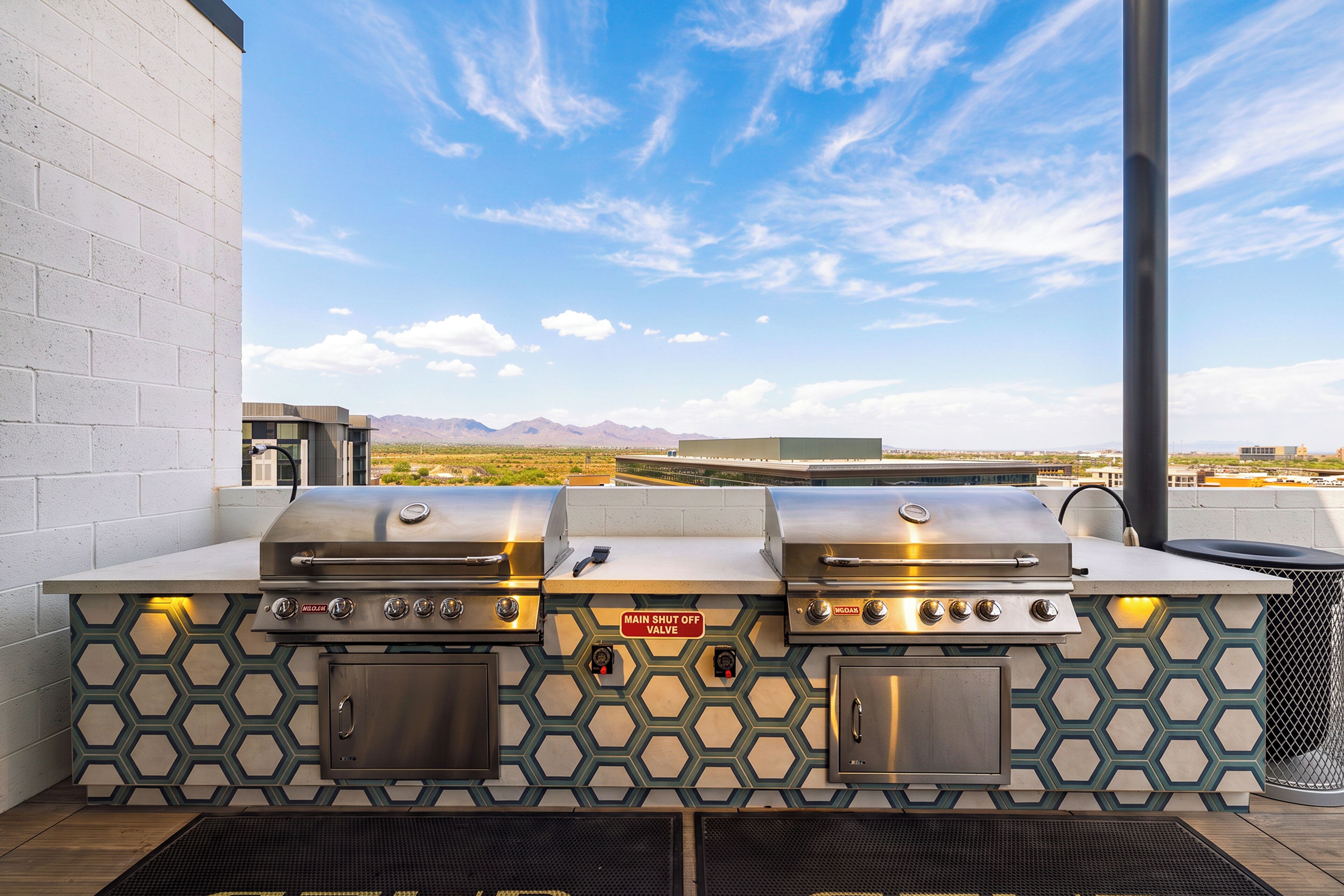 An outdoor grill station with two gas grills, a built-in cooler, and a view of the desert landscape.