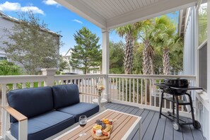 A covered outdoor seating area with a sofa, a table with a wine glass and food, and a grill cart. - Golf Cart + Hot Tub + Community Pool | Near the Gulf | 78 Emerald (Santa Rosa Beach)