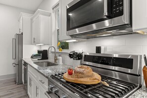 A modern kitchen with stainless steel appliances, a granite countertop, and a wooden cutting board with food items. - Golf Cart + Hot Tub + Community Pool | Near the Gulf | 78 Emerald (Santa Rosa Beach)