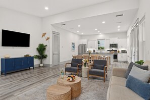 A modern living room with a flat-screen TV, a blue cabinet, and a dining area with a kitchen in the background. - Golf Cart + Hot Tub + Community Pool | Near the Gulf | 78 Emerald (Santa Rosa Beach)