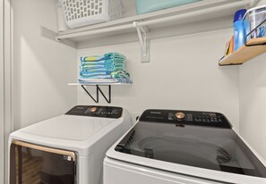 A laundry area with two washing machines, a drying rack, and a shelf with laundry items. - Golf Cart + Hot Tub + Community Pool | Near the Gulf | 78 Emerald (Santa Rosa Beach)
