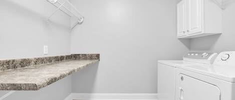 A laundry room with a granite countertop, a washing machine, and a drying rack.