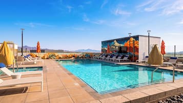 A pool area with lounge chairs, umbrellas, and a mural on the wall.