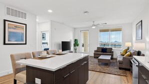 A modern apartment with a central island, a flat-screen TV, a dining area, a living room with a sofa and a coffee table, and large windows with a view. - North Scottsdale Condo • Shared Rooftop Pool + Spa + Sauna + Views | Azur #246 (Phoenix)