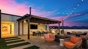 An outdoor patio area with a bar, seating, and a view of the mountains. - Rooftop Pool + Sauna & Spa | Near TPC Golf + Preserve | Azur (Phoenix)