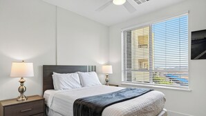 A bedroom with a bed, two bedside tables with lamps, a window with blinds, and a ceiling fan. - Rooftop Pool + Sauna & Spa | Mins to Desert Ridge + TPC Golf | Azur (Phoenix)