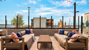 An outdoor seating area with sofas and a table, overlooking a cityscape. - Rooftop Pool + Sauna & Spa | Mins to Desert Ridge + TPC Golf | Azur (Phoenix)