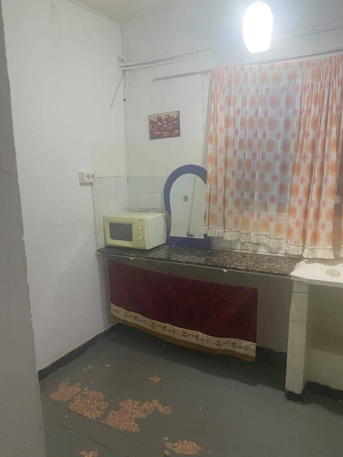 Una piccola cucina con un forno a microonde, un lavello e una finestra con tenda.