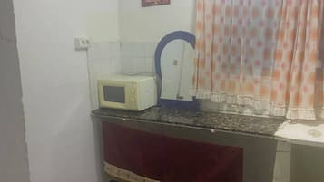 Uma cozinha compacta com micro-ondas, pia e janela com cortina.