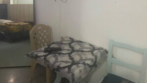 A room with a bed, a television mounted on the wall, a table with a patterned tablecloth, and a chair. - Dar Massmoudi (Tunis)