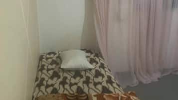 Um quarto pequeno com cama, travesseiro, cortina e uma tomada.