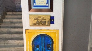 A reception area with a framed sign, a reception plaque, and a blue door. - Dar Massmoudi (Tunis)