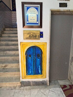 A reception area with a framed sign, a reception plaque, and a blue door. - Dar Massmoudi (Tunis)