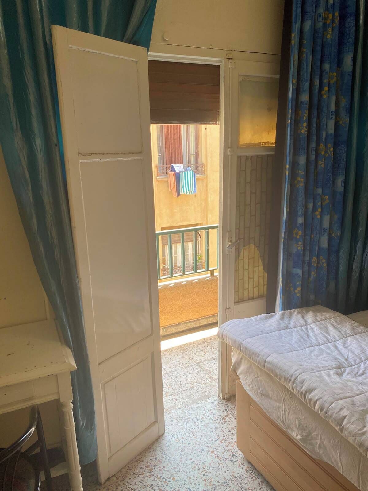 Um quarto com uma cama, uma porta que dá para uma varanda e uma cadeira.