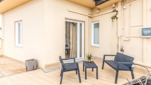 A building with a beige exterior, a tiled roof, and a patio area with two chairs and a small table.