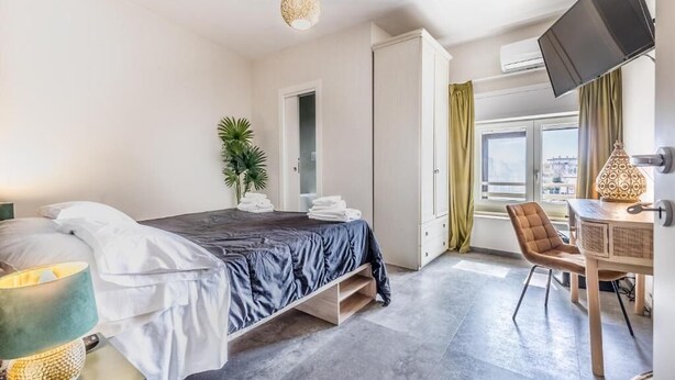 A hotel room with a bed, a desk, a chair, a TV, and a window with curtains.