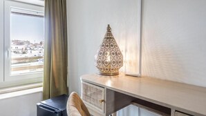 A desk with a decorative lamp, a window with a view of a cityscape, and a curtain.