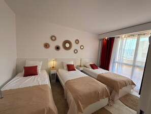 Une chambre d’hôtel avec trois lits simples, une grande fenêtre avec des rideaux et des miroirs décoratifs fixés au mur.